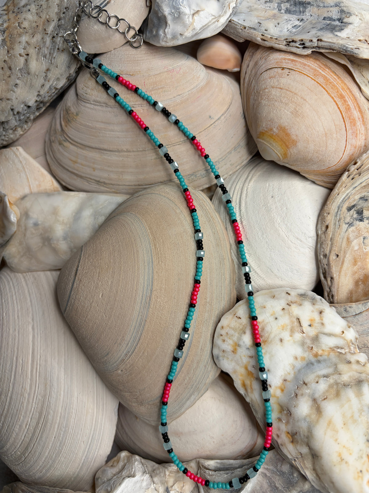 Untamed Tide beaded necklace in teal, coral pink, black, and sand-toned glass beads arranged on seashells